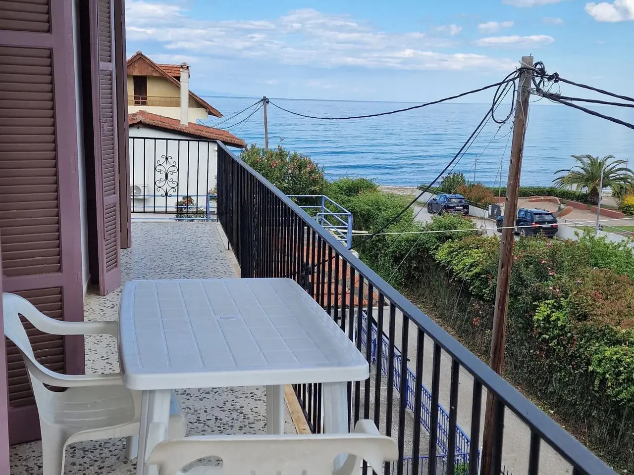 Balkon Apartmana 5 sa stolom i stolicama i pogledom preko obalskog puta na Egejsko more