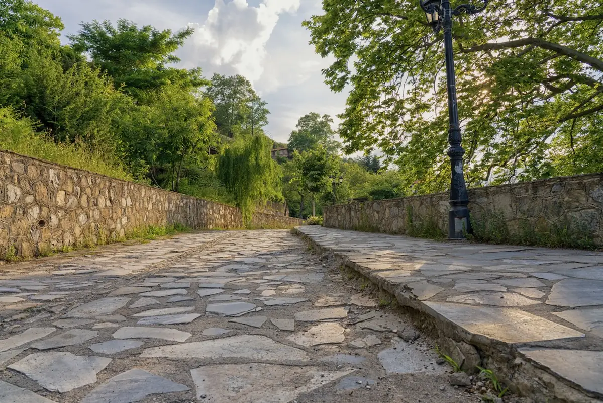 Cobbled lane in Palaios Panteleimonas with an old street lamp and dry-stone walls
                in the evening light