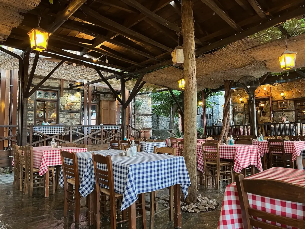Traditional taverna in Palaios Panteleimonas with a timber roof, lanterns and
                chequered tablecloths