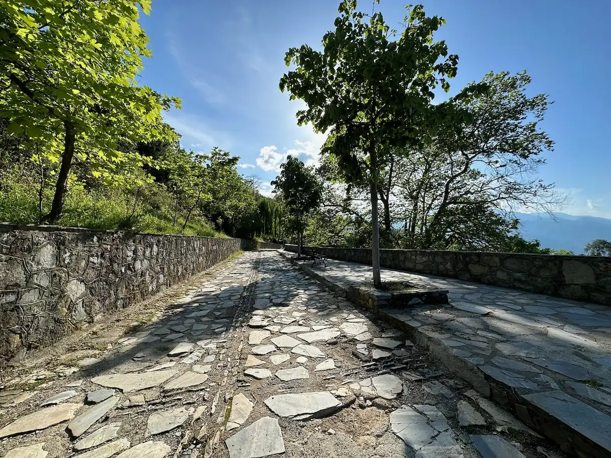 Wide cobbled path in Palaios Panteleimonas, lined with dry-stone walls and trees